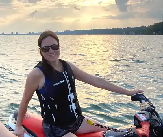 Cybele Gorrissen, sitting on a jetski, wearing a life jacket and sunglasses. A lake can be seen behind her