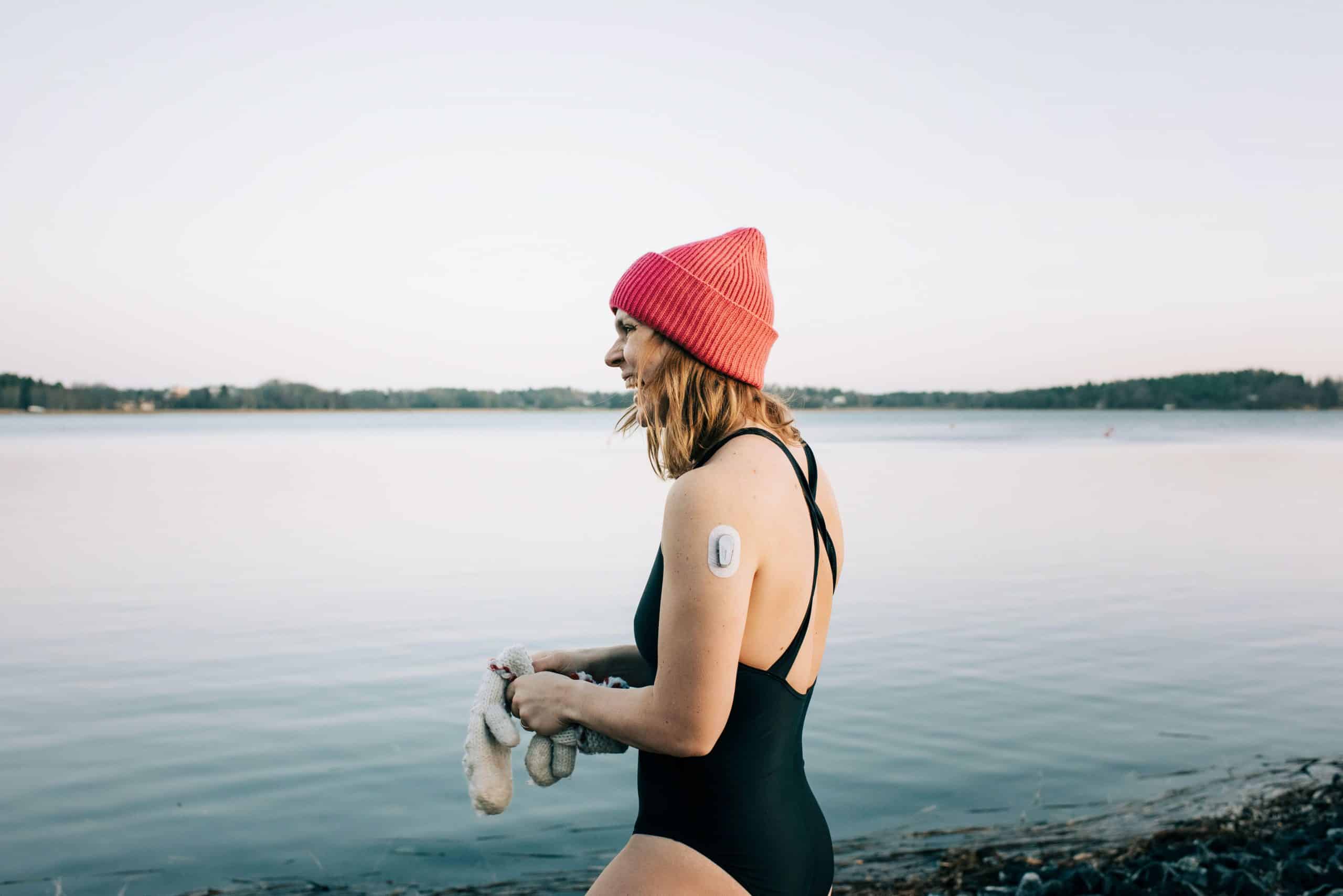 A woman wearing a bathing suit, a toque and a glucose monitor enters cold water for a polar dip.