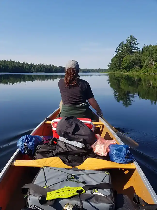 Katelyn Dewar, seen from behind wearing a black shirt and hat while she canoes on a lake