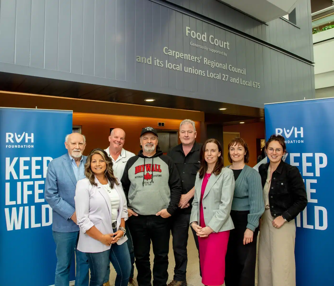 Representatives from the Carpenter's Regional Council and it's local union's 27 and 675 gather underneath their recognition sign in RVH's Food Court alongside members of Team RVH.
